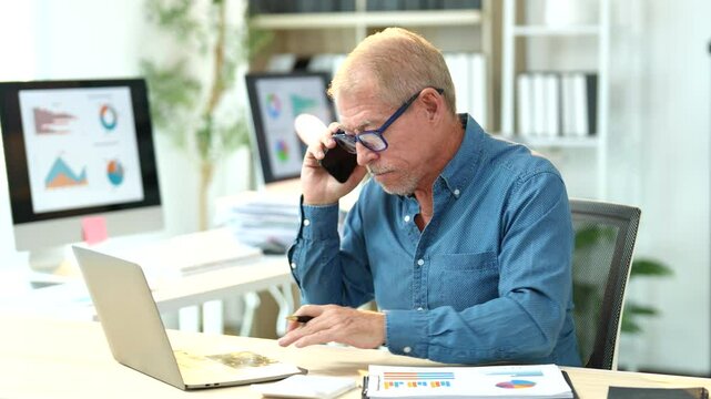 Senior professional multitasking during business call, analyzing financial reports on laptop while sitting at corporate workplace desk