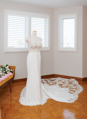 A mannequin in a wedding dress with a train in the bride's room. White wedding dress with sleeveless lace bodice and train on a full-length mannequin. The bride's dress in the room on the wedding day