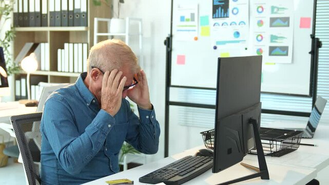 Stressed senior businessman massaging temples, experiencing intense migraine after prolonged computer work in corporate office environment