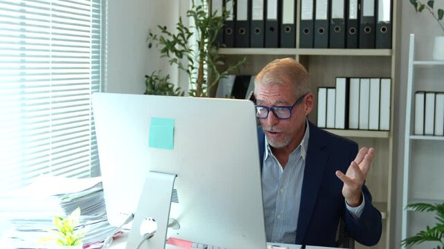 Professional businessman in formal suit communicating via video conference, making expressive gestures while working remotely on desktop computer