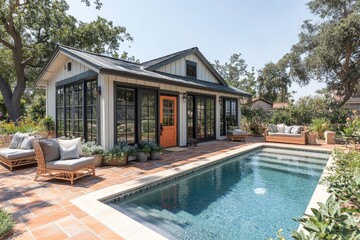 Fototapeta premium Small barn-style gray and white building with orange door next to in-ground pool on red brick patio, California backyard, daytime.