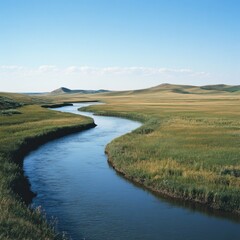 Fototapeta premium Serpentine river meandering through a vast, grassy prairie under a clear blue sky.