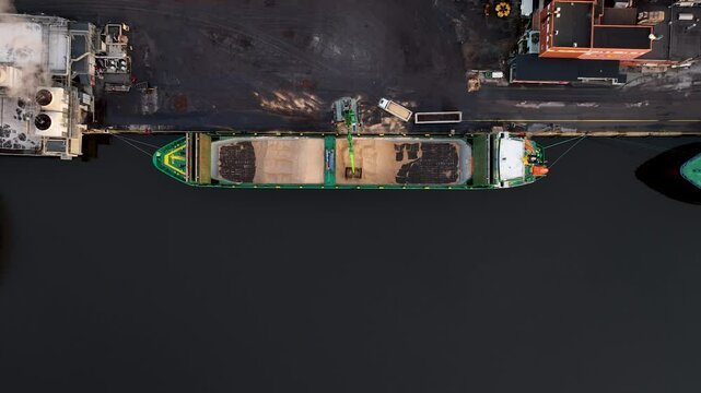 Cargo ship loading wood chip at industrial port paper mill