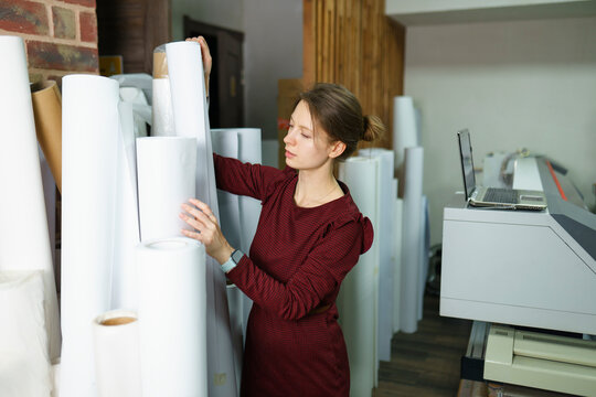 Woman removing roll of paper and standing near printer at printing studio
