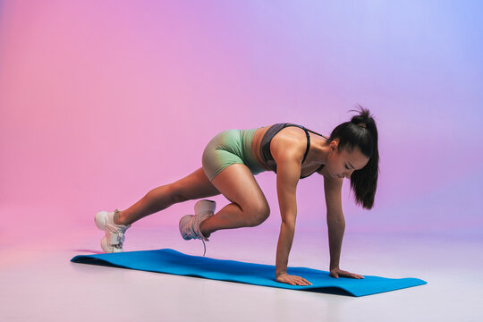 Young woman exercising on yoga mat against colored background - Powered by Adobe