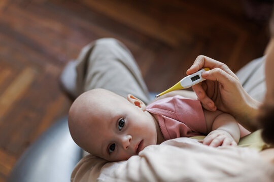Mother holding baby and checking fever with thermometer at home - Powered by Adobe