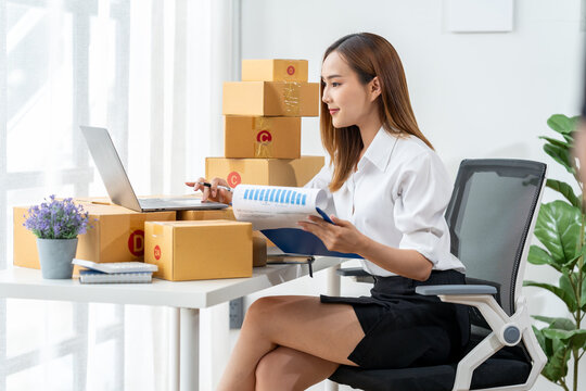 Focused on Growth: An empowered businesswoman meticulously reviews a document in her home office, surrounded by packages, showcasing the dynamic world of online entrepreneurship. 