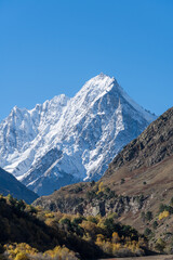 View of snow-capped peaks of Chegem Gorge. Kabardino-Balkaria. Majestic natural landscapes of Elbrus region against backdrop of blue autumn sky. Steep cliffs covered in snow and ice rise upward.