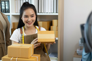 A woman is holding a brown cardboard box with a white ribbon tied around it. She is smiling and she is happy
