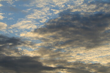 The sky is light blue with white and gray clouds. The clouds seem to spread across the sky. The sunlight shines down on the clouds, making them look soft. The sky looks peaceful.