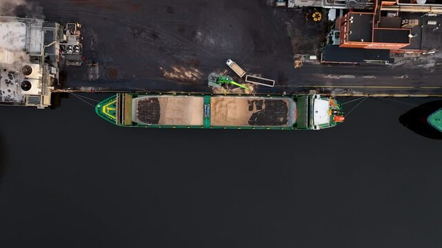 Crane loading cargo wood chip ship at industrial port paper mill