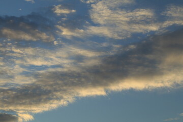 The sky is light blue with white and gray clouds. The clouds seem to spread across the sky. The sunlight shines down on the clouds, making them look soft. The sky looks peaceful.