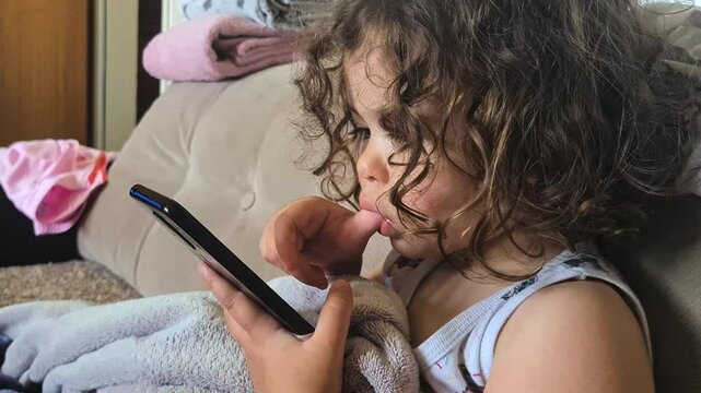 Three Year Old Girl Scrolling Content on Social Media While Sucking Thumb in Mouth
