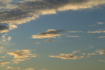 The sky is light blue with white and gray clouds. The clouds seem to spread across the sky. The sunlight shines down on the clouds, making them look soft. The sky looks peaceful.