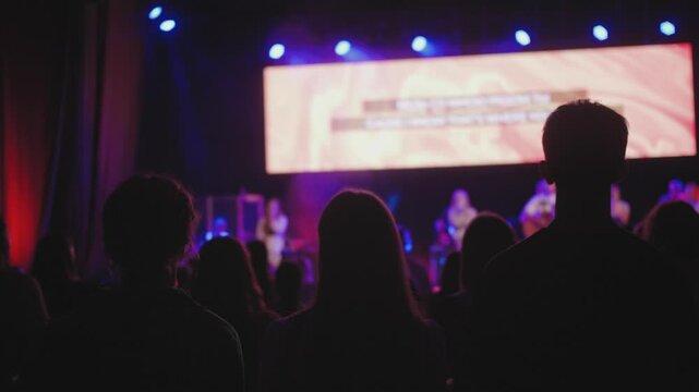 Young girl lifting hand up during christian worship night performing, christian band on the stage singing and playing musical instruments, worshipping God Lord with a crowd, raising hands at concert