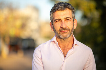 Thoughtful man outdoors with neutral expression and blurred background