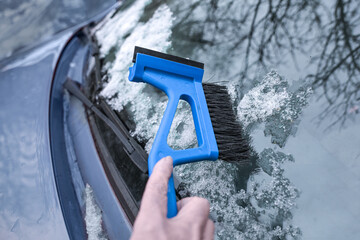 Hand sweeping snow from the car windshield with an ice scraper and broom, important winter tool for...
