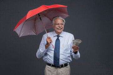 A Grey-Haired Indian Old Man Laughing While Holding An Umbrella And Indian Currency�