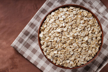 Raw Rolled Oats in Clay Bowl on Checkered Linen Napkin, Top View, Copy Space