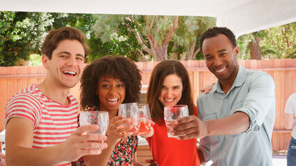 Portrait Of Group Of Young Friends Doing Cheers To Camera With Drinks Outdoors In Garden At Home