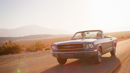 Two Young Female Friends On Road Trip Driving In Classic Convertible Car On Country Road