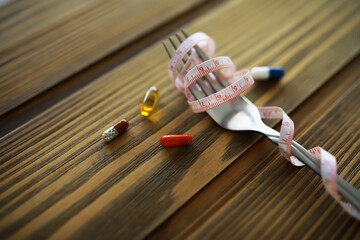 Fork with Measuring Tape and Pills on Wooden Table: Concept of Diet and Health