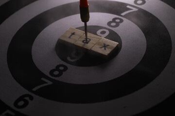 Dart Hitting the Word 'Tax' on Scrabble Tiles at the Center of a Target Bullseye in Dark Lighting