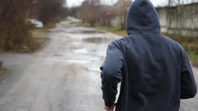 Young sportsman jogging along rural trail at cloudy day. Athletic sporty man running along country road in the rain. Strong athlete doing cardio training outdoor. Healthy active lifestyle. Close up
