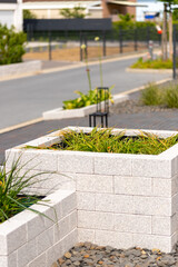 Raised bed made of natural stone bricks with grass as content, street in the background