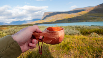 Enjoying coffee in traditional wooden crafted mug called kuksa in the middle of Lapland nature evokes beautifully spent time in the wilderness and enjoy friluft culture. Kungsleden trail, Sweden.