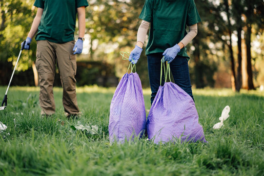 Two volunteers collecting garbage in park are holding trash bags
