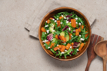 Sweet potato salad with arugula, avocado, cucumber and veta cheese in wooden bowl on light background. Healthy food top view. Food background with copy space