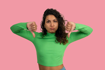 Young woman showing thumbs down gesture expressing dislike on pink background