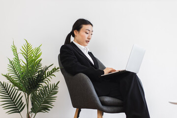 Asian businesswoman wearing black suit sits chair using laptop. Indoor professional work...