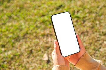 Mockup image of a woman holding mobile phone with blank white desktop screen in the outdoors