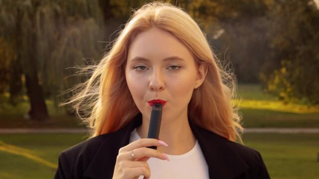 Young pretty woman standing outside street having break smoking trendy tobacco device electronic cigarette heater vape. Smoke and steam system with sticks inside. Harmful habit harm to health lungs
