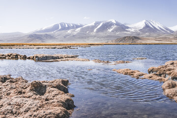 Panorama of a high-mountain landscape, a lake and a river in the mountains flows in a mountain valley among meadows against the background of mountains, landscape in the Pamir Mountains background