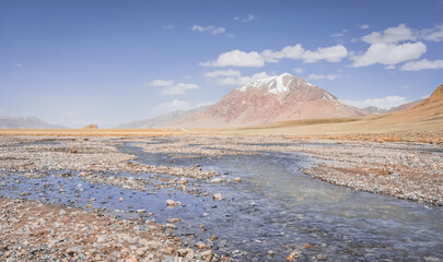 High-mountain river flows in a valley against the background of rocky mountain ranges in the Tien Shan mountains in the Pamirs in Tajikistan, landscape for background