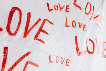 Multiple drawings of the word LOVE hand-painted in bright red forming a pattern on a plain white surface oilcloth, Valentine`s day concept celebration decoration in photo studio. Love, holiday, party