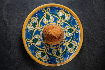 Traditional crispy Sicilian arancino or arancina on a typical colorful handmade decorative plate