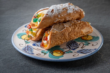 A stack of freshly prepared Sicilian cannoli with ricotta and candied fruit on a traditional handmade ceramic plate