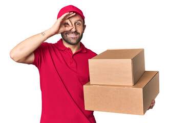 Hispanic male courier with boxes excited keeping ok gesture on eye.