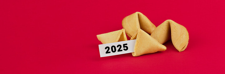Fortune cookies with one revealing year 2025 on slip of paper, arranged on bold red background with...