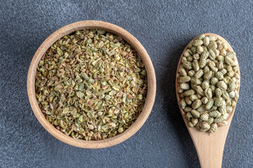 A bowl filled with a pile of natural dried thyme seeds, alongside a spoon containing ground thyme
