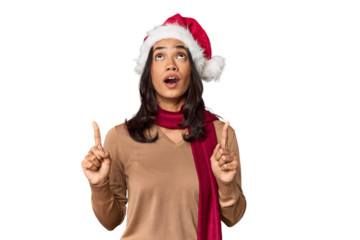 Filipino in Christmas attire and Santa hat pointing upside with opened mouth.