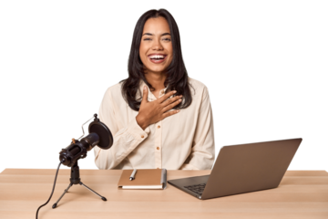 Woman records podcast with laptop laughs out loudly keeping hand on chest.