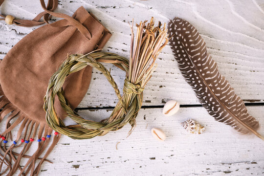 Sweetgrass braid (Hierochloe odorata), also called vanilla grass, on a medicinal pouch and smudging feather on old white wood. Overhead view.