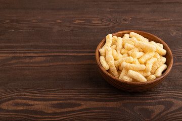Corn flakes sticks with caramel in wooden bowl on brown wooden, side view, copy space.