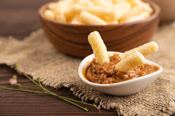 Corn flakes sticks with caramel in wooden bowl on brown wooden, Side view, close up, selective focus.