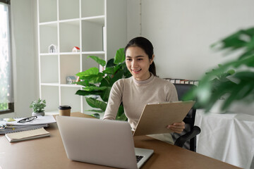 Professional Businesswoman Working Remotely in Modern Office with Laptop and Clipboard, Surrounded...
